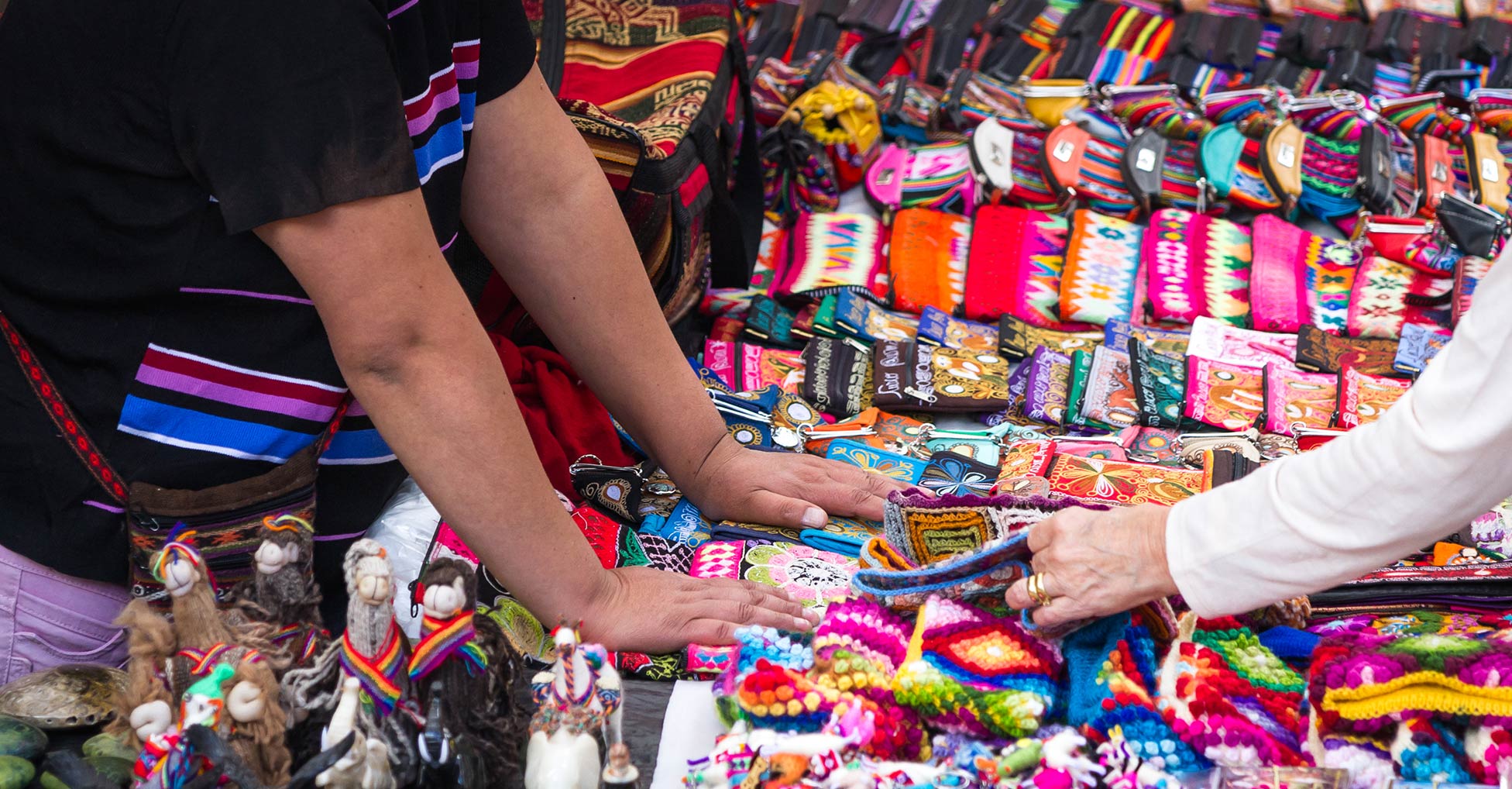 Two sets of hands touch artisan handicrafts displayed on a table
