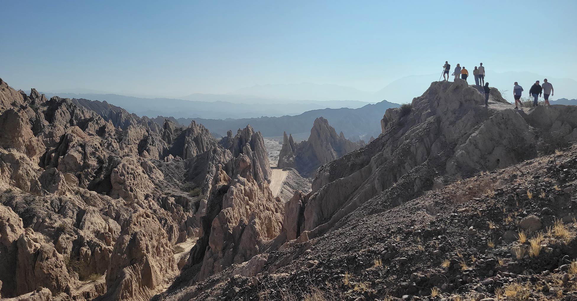 A landscape with jagged, rocky formations and several people hiking in the distance