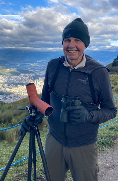 Portrait of Eric Moore outdoors, with binoculars and a scope