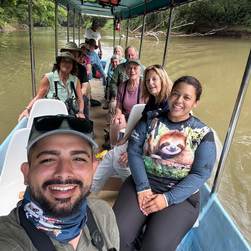 Twelve people and a boat driver smiling on a small boat on a river.
