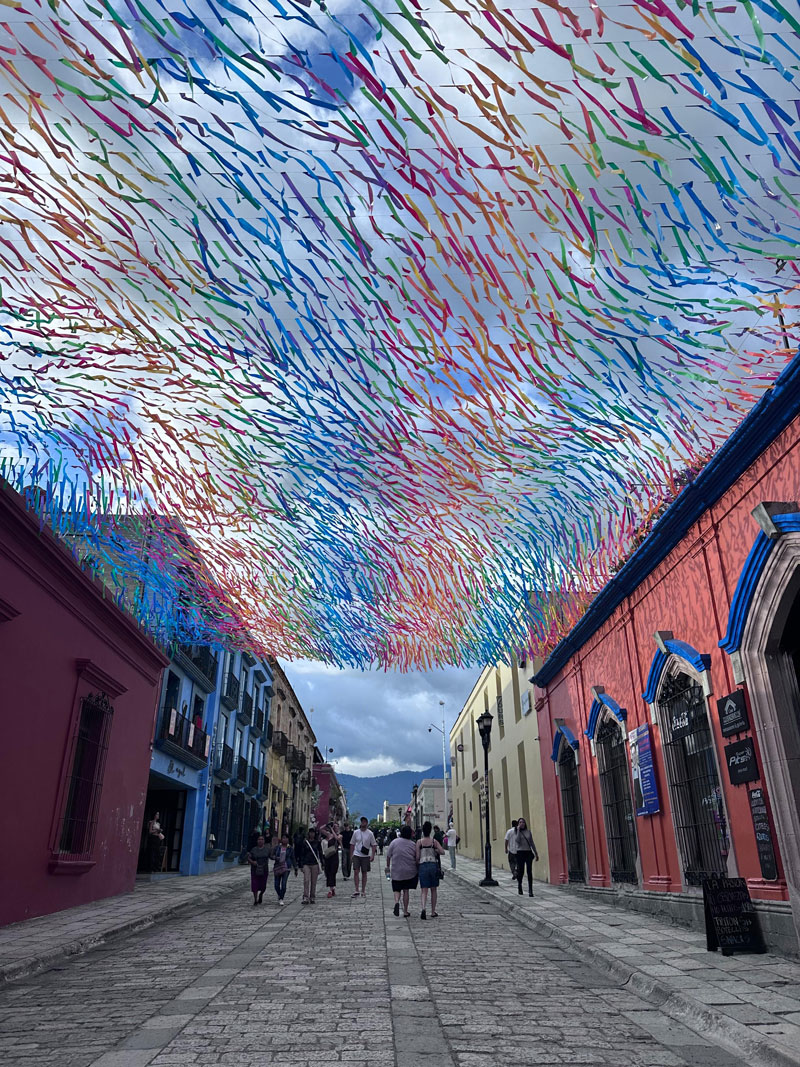 A cobblestone street Spanish colonial-style buildings on either side and colorful streamers strung above.