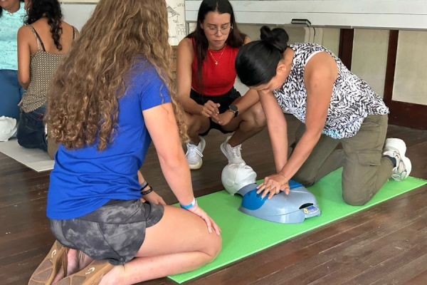 A person practices CPR on a dummy while two other people watch.