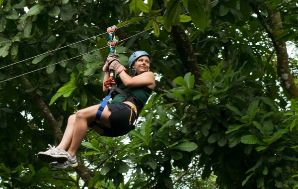 A teenager or young adult zip lines through the rainforest canopy