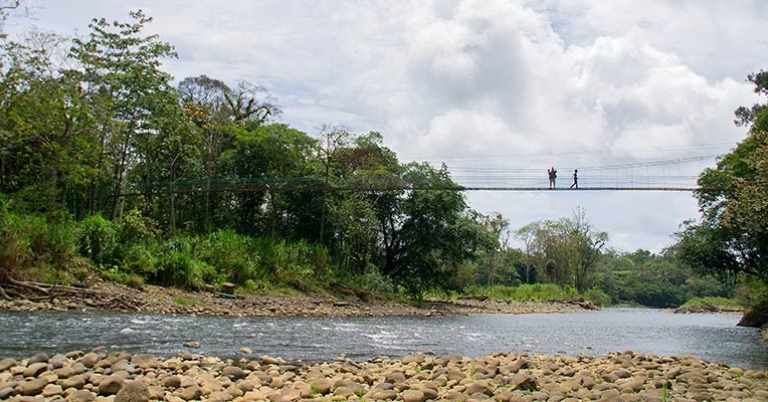 Two people stand on a suspension bridge over a river