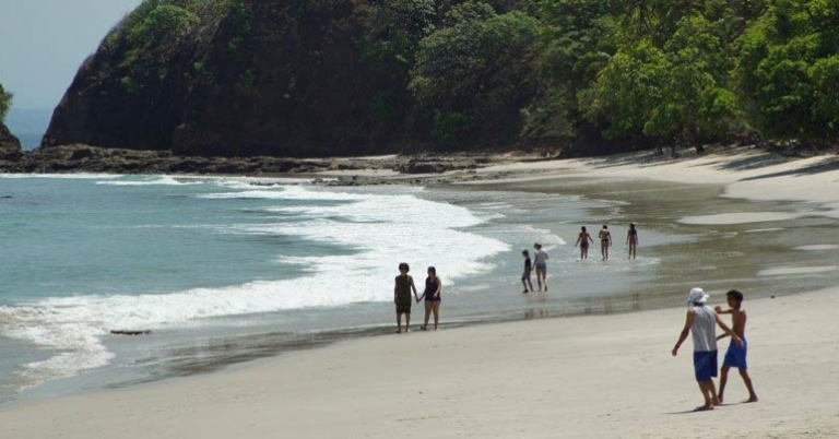 several groups of tourists walk along the beach