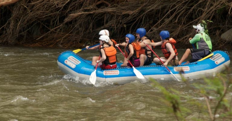 Group of five students and a guide sit in a raft on the river