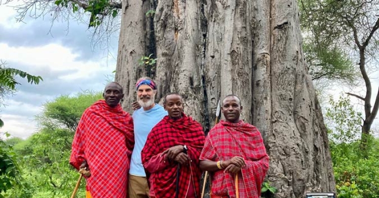 Three Maasai men wearing traditional clothing standing with trip leader Kevin Stockmann in front of a large baobab tree