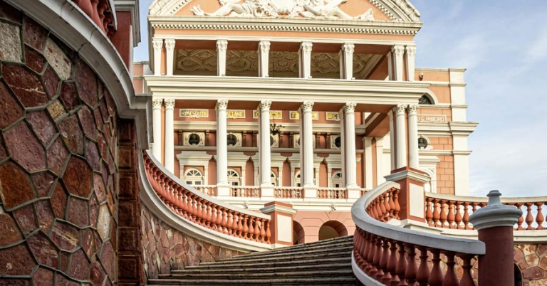 A curved stone staircase leads toward the exterior of an ornate multi-story building with columns