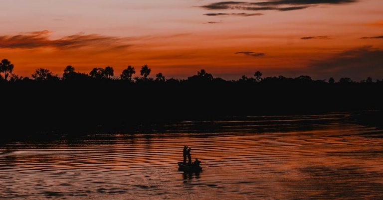 A fishing boat is silhouetted on a river with a darkening sky in the background
