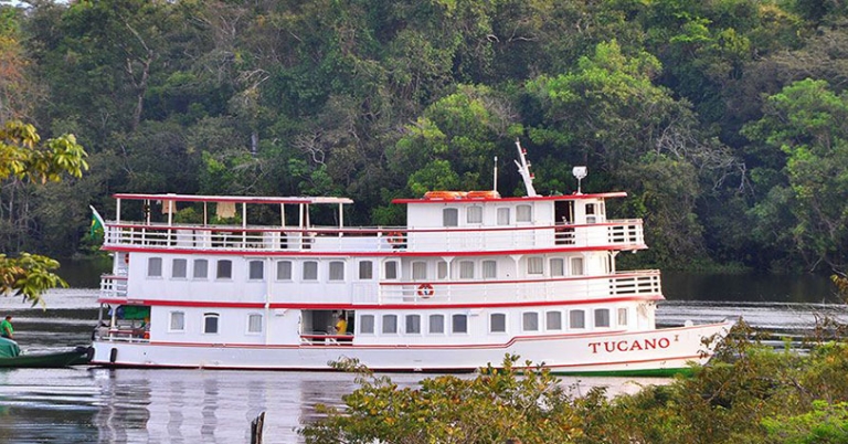 A riverboat cruises on a river with trees in the background