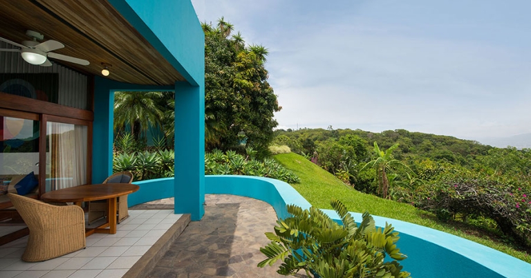 A tile patio with table and chairs and a low, curved wall overlooks lush vegetation