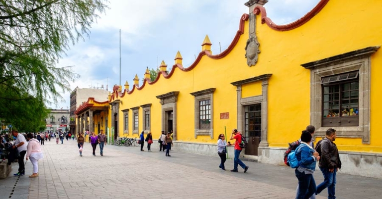 A few groups of tourists strolling in front of a brightly colored building