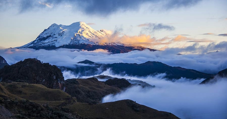 Snow-topped volcano with hills and low-lying clouds in foreground