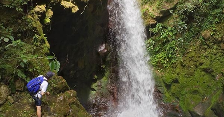 Three people stand on rocks overlooking a tall waterfall