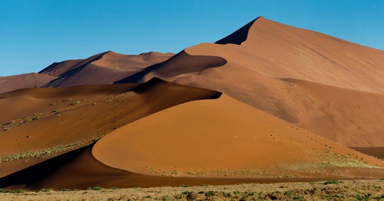 A sand dune, several hundred feet high, towers over a flat landscape with low grass and shrubs