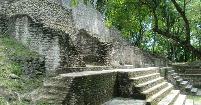 A multilevel limestone temple with stairs, shaded by trees