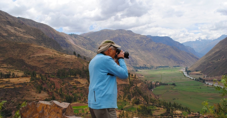 A photographer takes a picture of a valley with a river and farmland and surrounded by mountains