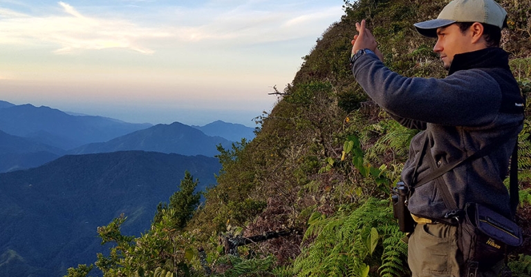 A person takes a picture of a mountainous landscape in early morning light