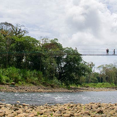 Two people stand on a suspension bridge over a river