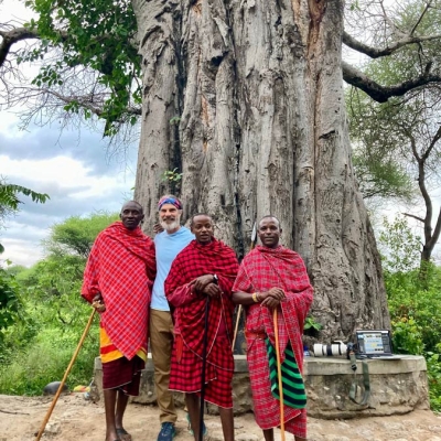 Three Maasai men wearing traditional clothing standing with trip leader Kevin Stockmann in front of a large baobab tree