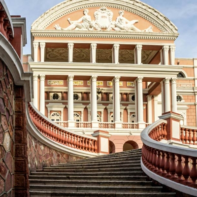 A curved stone staircase leads toward the exterior of an ornate multi-story building with columns