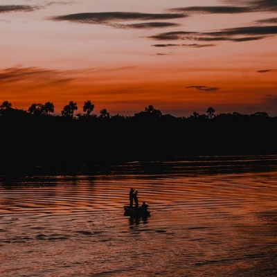 A fishing boat is silhouetted on a river with a darkening sky in the background