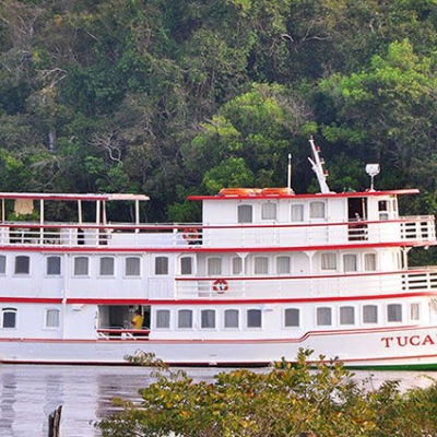 A riverboat cruises on a river with trees in the background