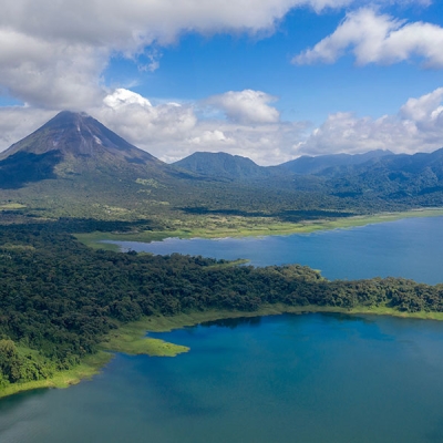 Aerial view of a lake surrounded by forest, with a volcano and low mountains in the background