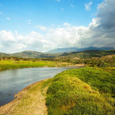 Panoramic view of a wide river with vegetation on the banks and low mountains in background