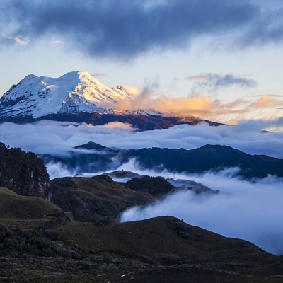 Snow-topped volcano with hills and low-lying clouds in foreground