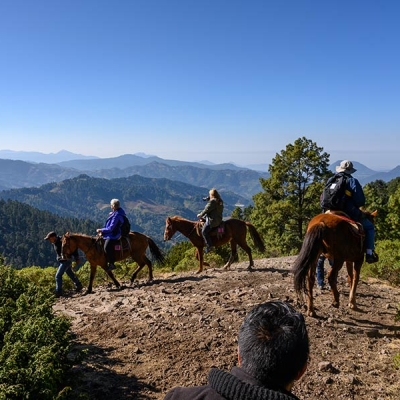 Three people ride horseback near an overlook with a mountainous landscape in the background