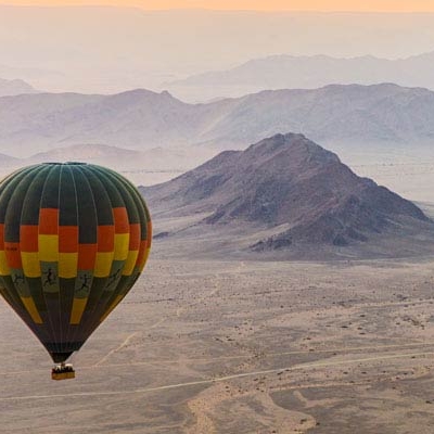 A hot air balloon floats in the sky over a desert landscape with low mountains in the background