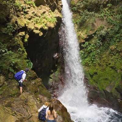 Three people stand on rocks overlooking a tall waterfall