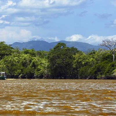 A small boat on a wide river, with trees and low mountains in the background