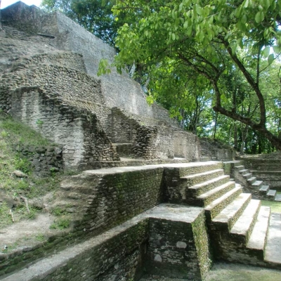 A multilevel limestone temple with stairs, shaded by trees