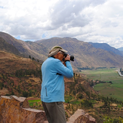 A photographer takes a picture of a valley with a river and farmland and surrounded by mountains