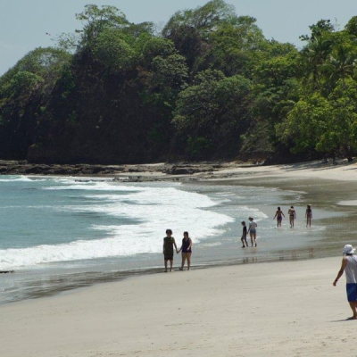 Several small groups of people walk on a sandy beach near the ocean