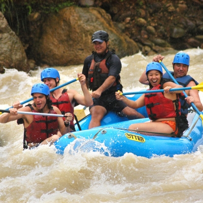 Four people and a guide hold oars while sitting in an inflatable raft on a river with small waves
