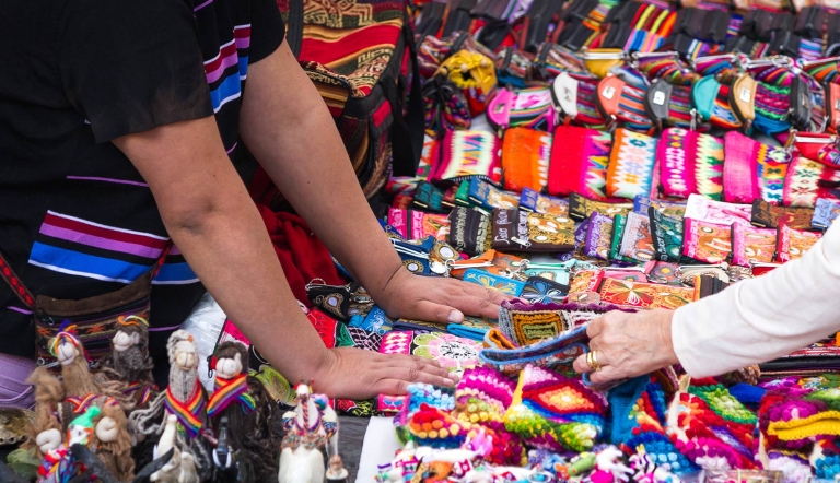 Two sets of hands touch artisan handicrafts displayed on a table