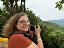 A woman smiling and holding a camera on a scenic overlook