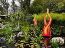 Pond surrounded by lush vegetation and a fire sculpture at Quito Botanical Garden