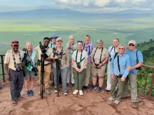 Twelve travelers and guides pose on a platform overlooking a vast valley below