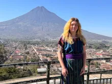 Staff member Jamie DeVoe poses on an overlook with a volcano and town in the background