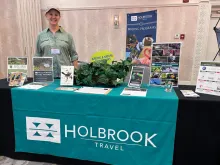 Staff member Jill Hays standing behind a conference table decorated with Holbrook-branded signs and handouts.