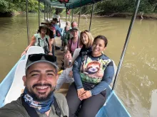 Twelve people and a boat driver smiling on a small boat on a river.